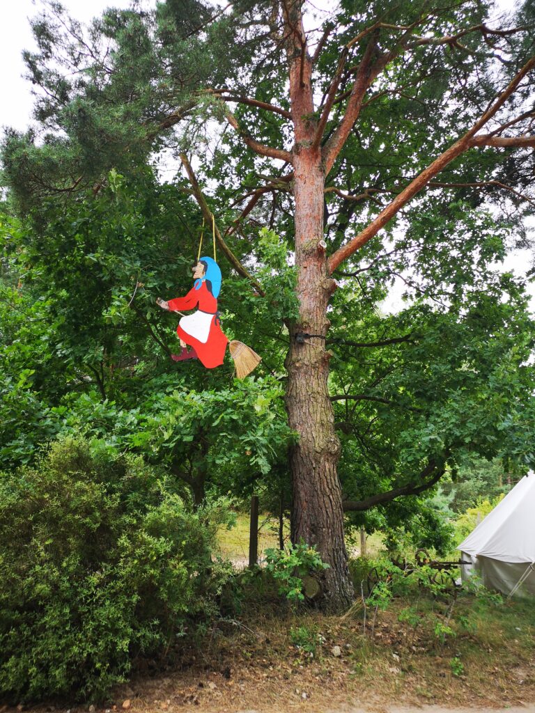Eine Holzhexe hängt am Eingang zum Zeltplatz in den Bäumen und reitet auf einem Besen