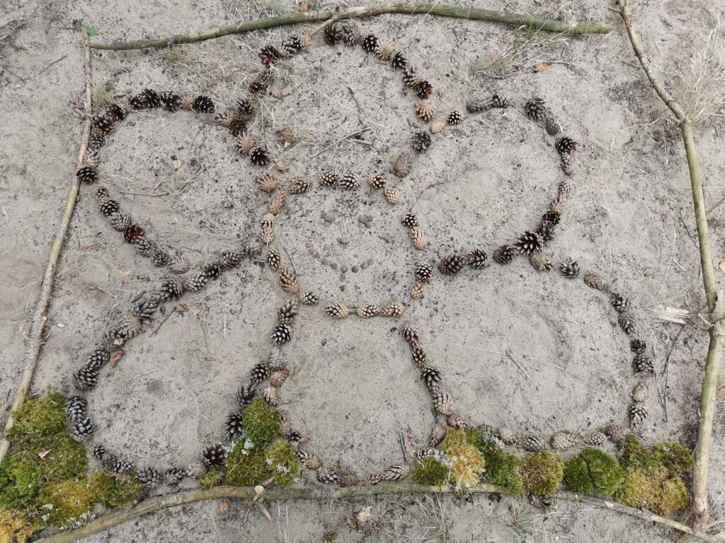 Aus Kiefernszapfen gestaltete Blume mit Gesicht im Sand