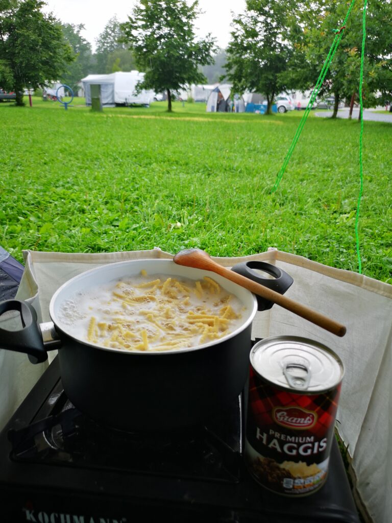 auf einem Campingkocher steht ein Topf in dem Spätzle kochen und daneben eine Dose Haggis, die noch mit rein kommt