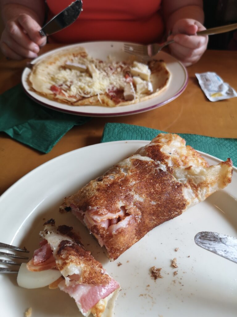 vor uns liegt ein eingerollter Eierkuchen auf einem Teller.
Dieser ist mit Speck und gekochtem Ei gefüllt