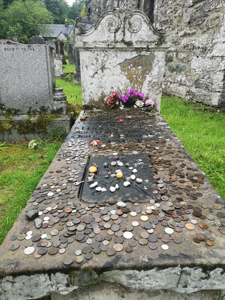 Grabstein und Grabplatte von Robert Kirk auf dem Friedhof in Aberfoyle Die Grabplatte ist überall mit Münzen und kleinen geschliffenen Steinen belegt