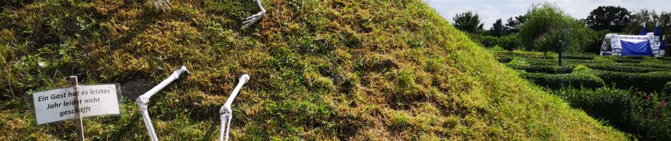 Auf einem Hügel wurde ein künstliches Skelett halb vergraben am Eingang zum Irrgarten